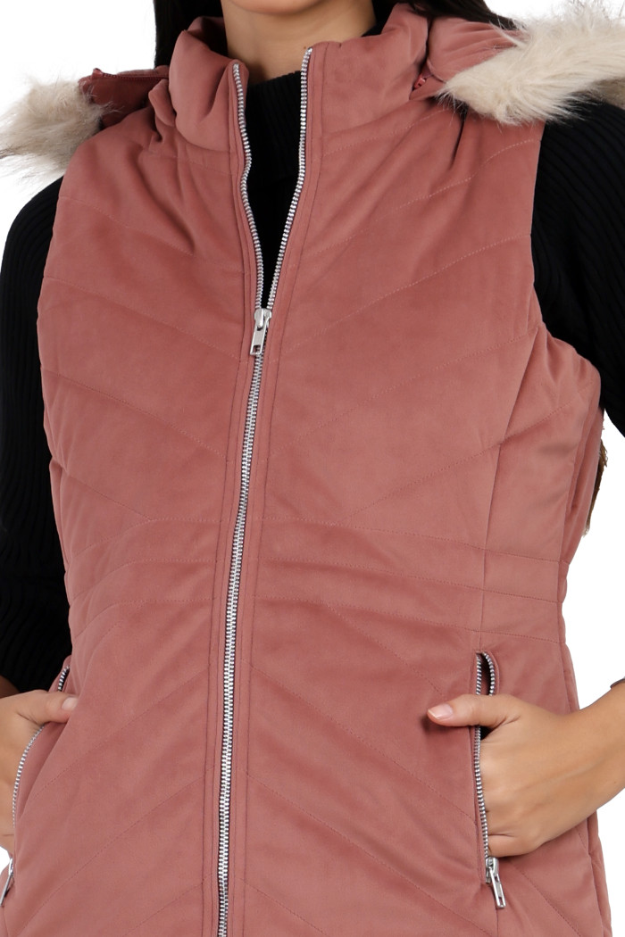 A cropped shot of a woman wearing Coatsnmore’s half sleeves jacket in onion pink colour with a textured pattern, removable hood with faux fur trim, side zippered pockets and a zip closure with her hands in the pocket.